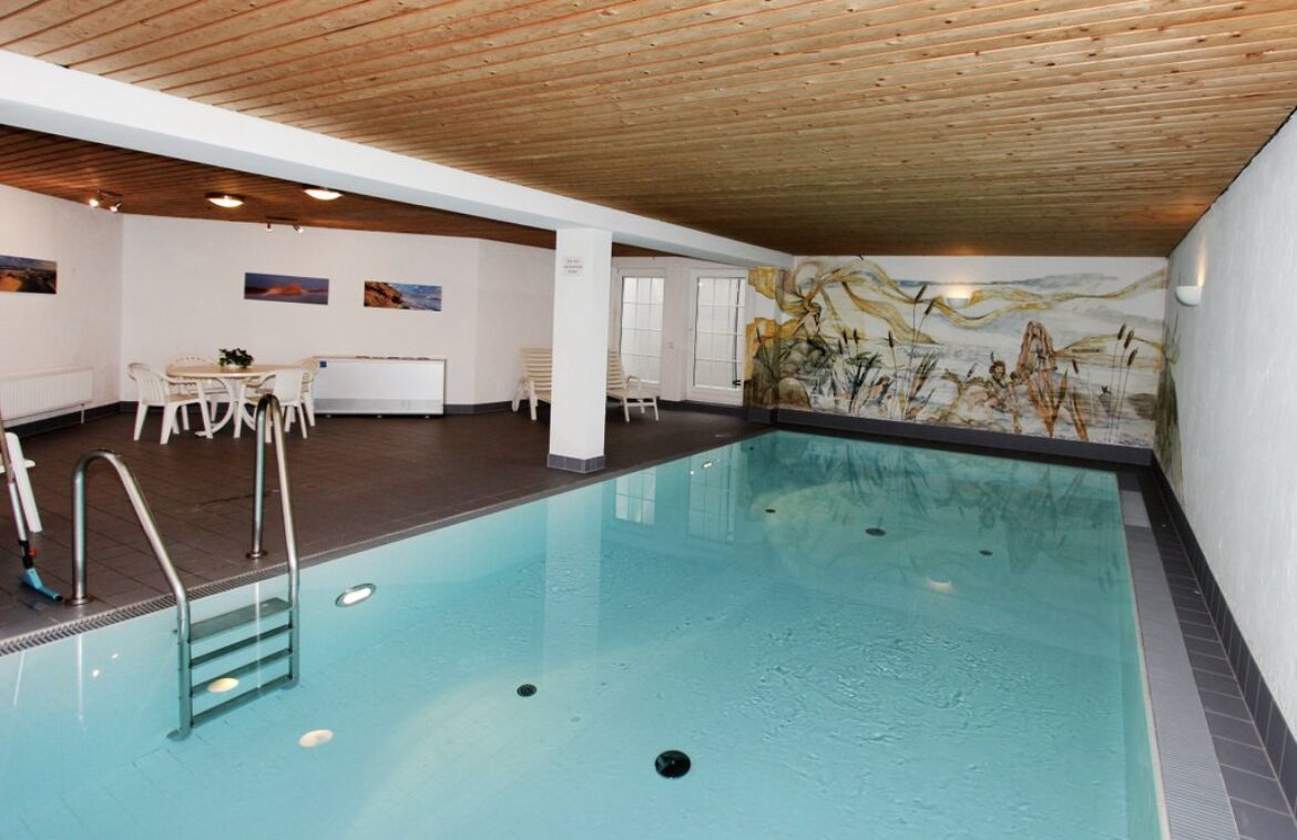 Ein Hallenbad mit Holzboden, Wandgemälde und einer Sitzecke mit Stühlen und Tisch.