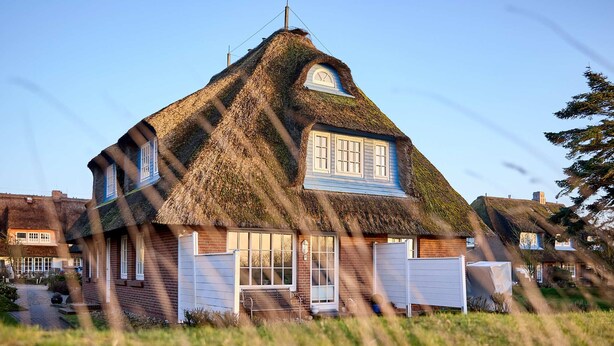 Une maison avec un toit de chaume, un porche à l’avant et une porte de garage bien visible.