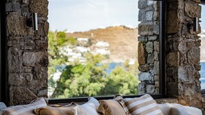 A bed with striped pillows, a stone wall, and a view of a coastal village.