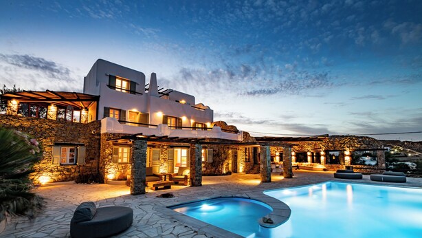 A modern villa with a swimming pool, stone walls, and outdoor seating.