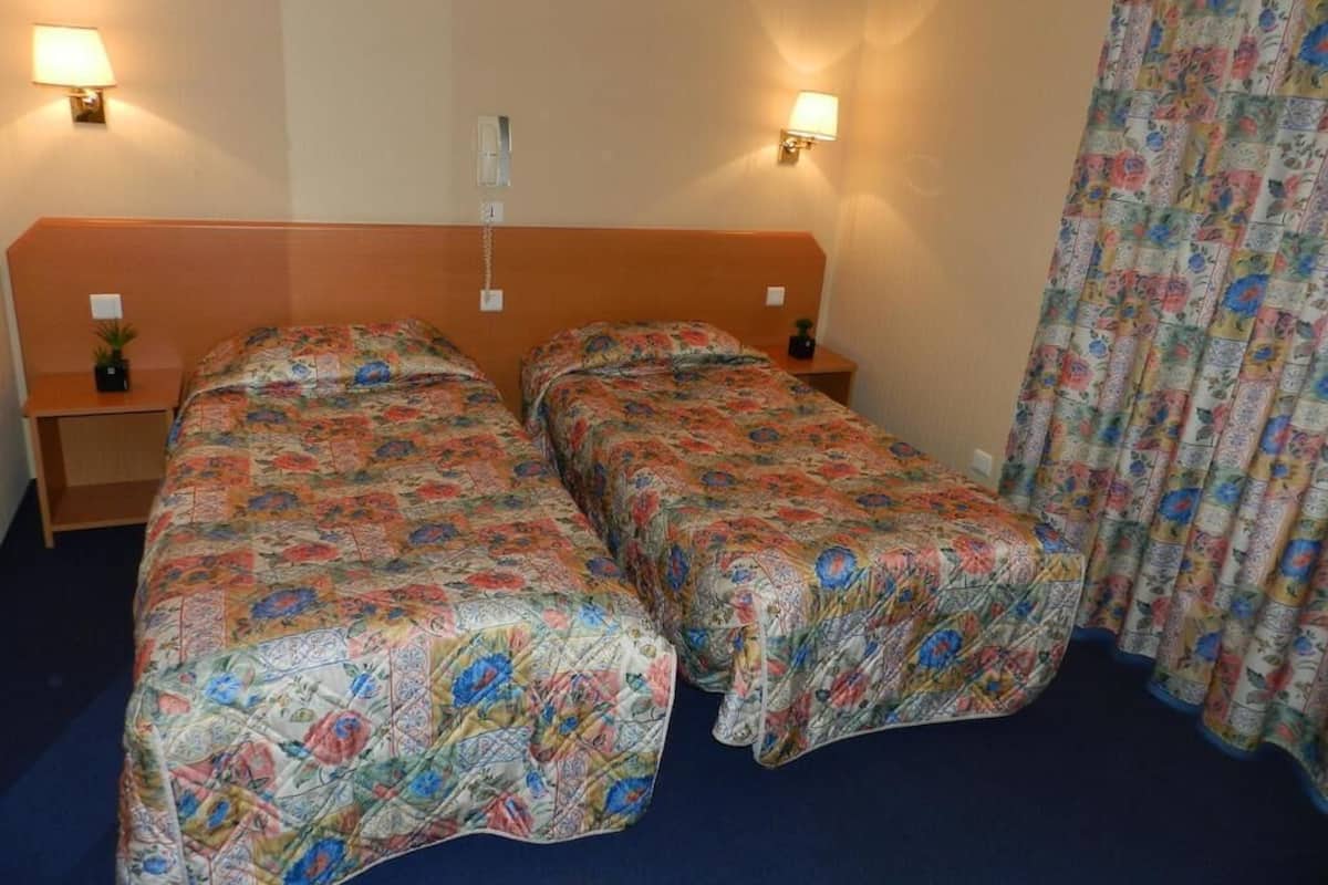 Habitación doble con dos camas individuales, cada una con cubrecama floral, lámparas de noche y mesita de noche con una planta pequeña.
