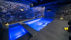 A spa area with a stone wall, a large rectangular hot tub, and candles. - Hotel Les Pardines 1819 (Encamp)