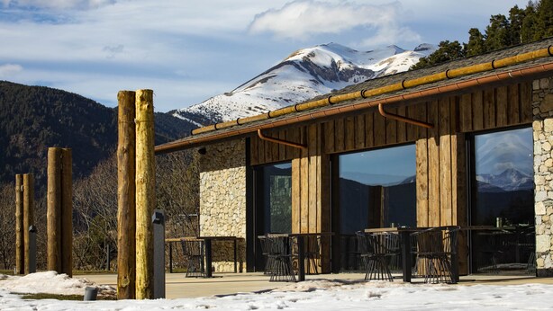 A building with large windows and a wooden exterior, overlooking a snowy mountain. - Hotel Les Pardines 1819 (Encamp)