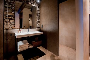 A modern bathroom with a stone wall, a white sink, and a mirror. - Hotel Les Pardines 1819 (Encamp)