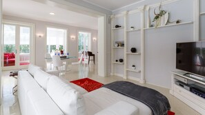 Un salon moderne avec un canapé blanc, un téléviseur à écran plat et un coin repas comprenant une table et des chaises en verre.