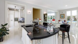 A modern kitchen with a black granite countertop, a coffee machine, and a scale. There is a glass bar counter with a seating area and a view of a pool outside. - Villa Guidi 10, Emma Villas (Cervia)