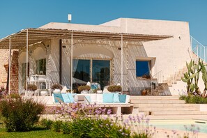 A modern villa with a pool, outdoor seating, and a staircase leading to a balcony.