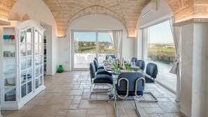 A dining area with a table set for six, a glass cabinet with dishes, and a view of the countryside through large windows. - Villa Gialonia 8+2, Emma Villas (Salve)