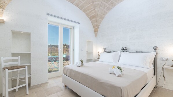 A bedroom with a large bed, a chair, and a balcony with a view.