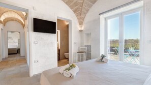 A bedroom with a large bed, a TV mounted on the wall, and a balcony with outdoor seating.