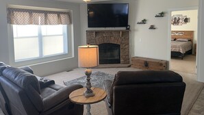 A living room with a fireplace, a flat-screen TV, a ceiling fan, and a sofa. - Hideout Haven (Baraboo)