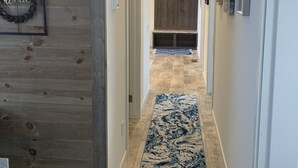 A hallway with wooden walls, a blue and white patterned rug, and a door with a 'blessed' sign. - Hideout Haven (Baraboo)