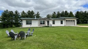 A two-story mobile home with a garage, a grassy yard, and a row of Adirondack chairs. - Hideout Haven (Baraboo)