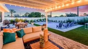 An outdoor patio with a wooden ceiling, a sofa with cushions, a table with a plant, and a pool area with lounge chairs. - Luxury 5BR Old Town Villa with Heated Pool & Games (Scottsdale)