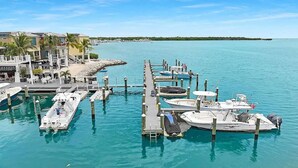 Un port de plaisance avec des bateaux amarrés, une jetée avec un restaurant, et une plage en arrière-plan.