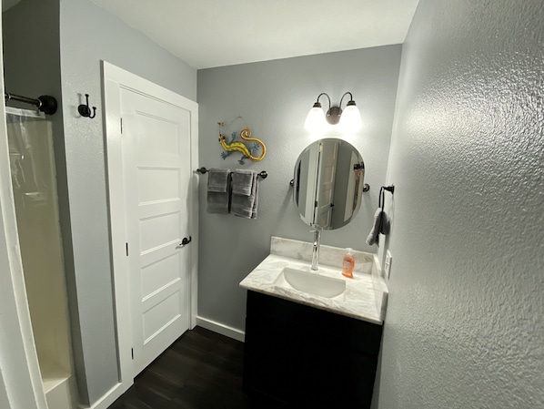 A bathroom with a white door, a mirror, a towel rack with towels, a soap dispenser, and a shower curtain.