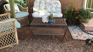 Un patio con mobiliario de mimbre, una mesa de metal y plantas en macetas.