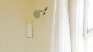 Ducha blanca con cortina, cabezal de ducha de mano y tres botellas de champú y acondicionador en un estante.