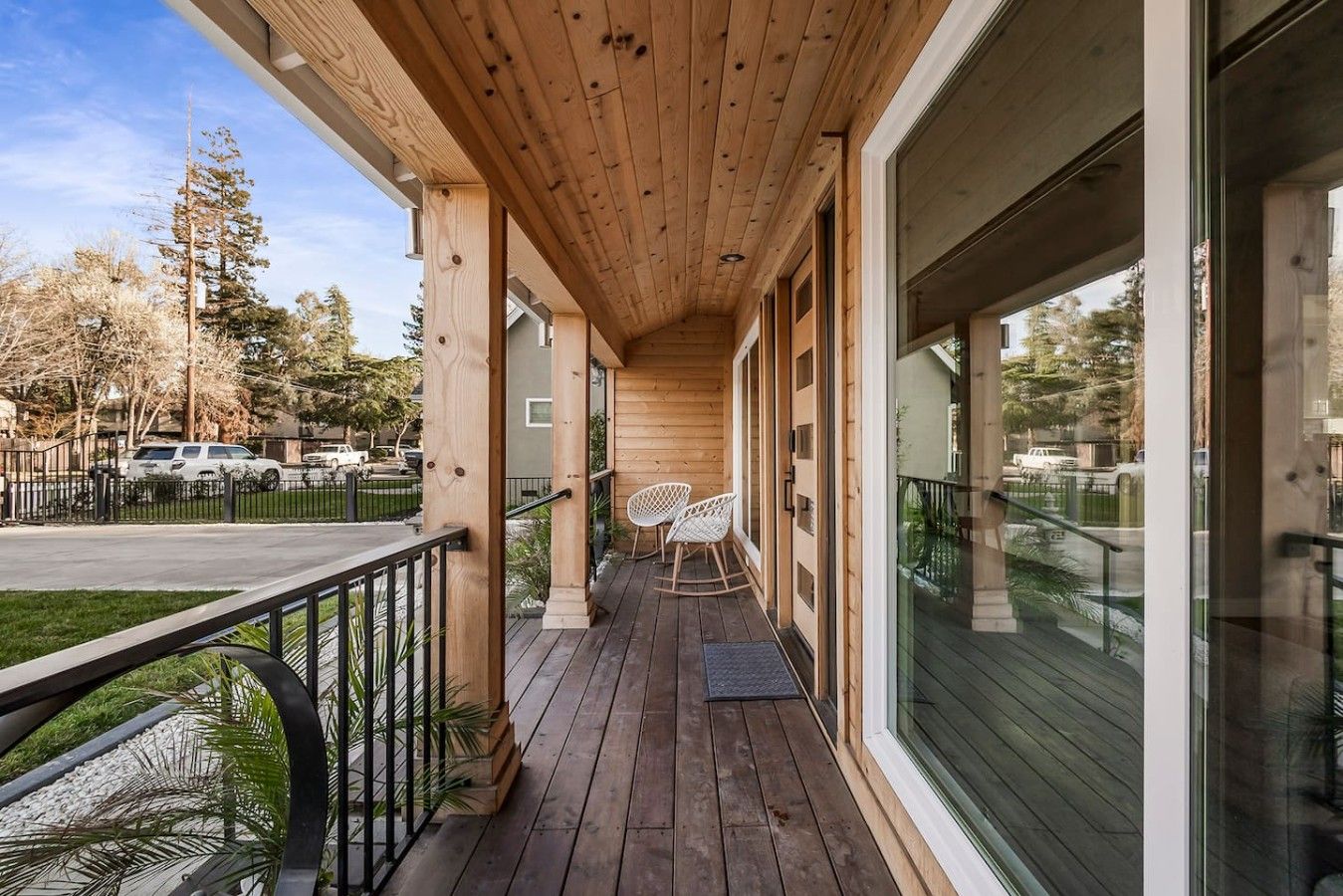 Une terrasse en bois avec une rambarde, deux fauteuils à bascule et une porte vitrée donnant sur un espace abrité.