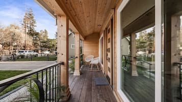 Une terrasse en bois avec une rambarde, deux fauteuils à bascule et une porte vitrée donnant sur un espace abrité.