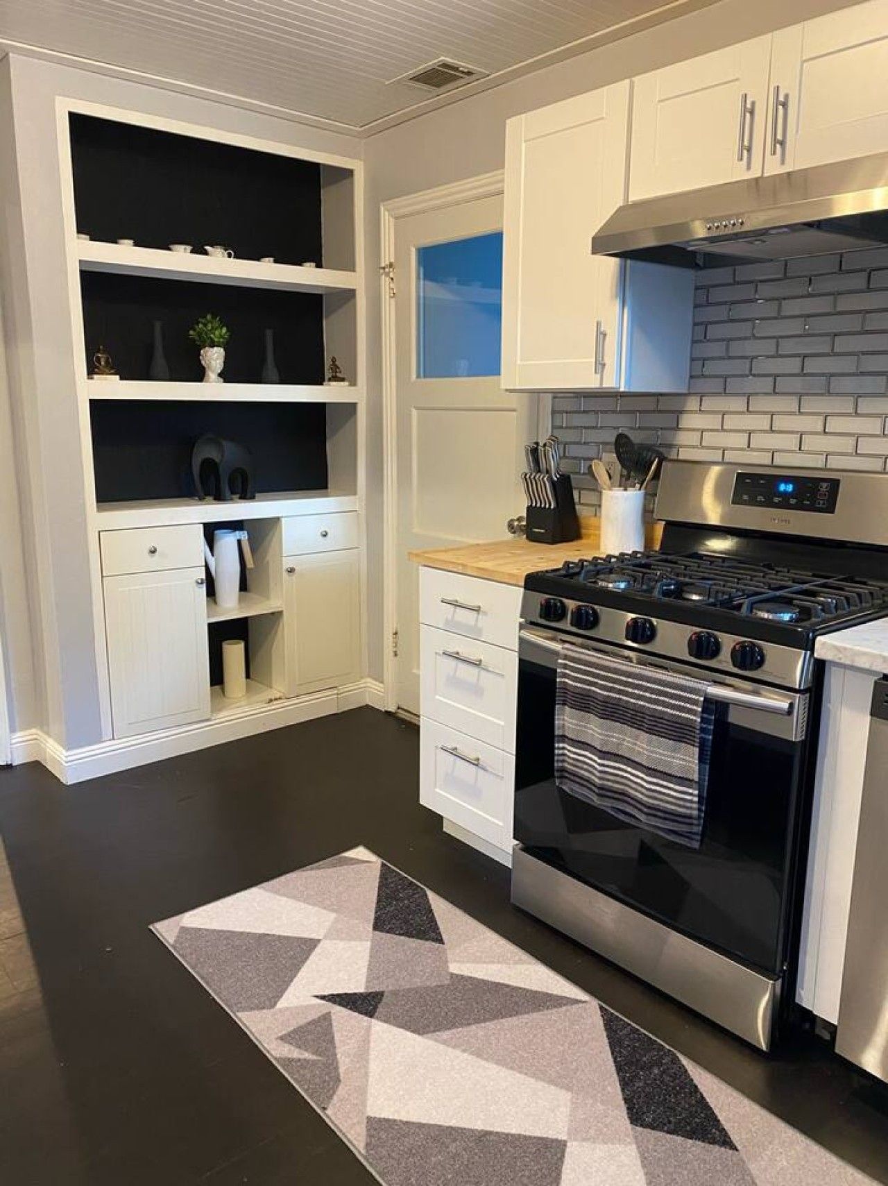 A modern kitchen with white cabinetry, a black and stainless steel stove, and a geometric patterned rug.
