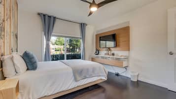 A bedroom with a bed, a ceiling fan, a TV mounted on the wall, and a window with curtains.