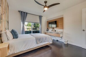 A bedroom with a bed, a ceiling fan, a TV mounted on the wall, and a window with curtains.