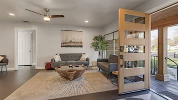 Uma sala de estar moderna com um sofá cinzento, uma mesa de centro original e uma porta de madeira que dá para uma área externa.