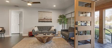Una sala de estar moderna con un sofá gris, una mesa de centro original y una puerta de madera que da a un espacio exterior.