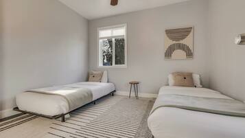 A bedroom with two beds, a window, a small stool, and a ceiling fan.