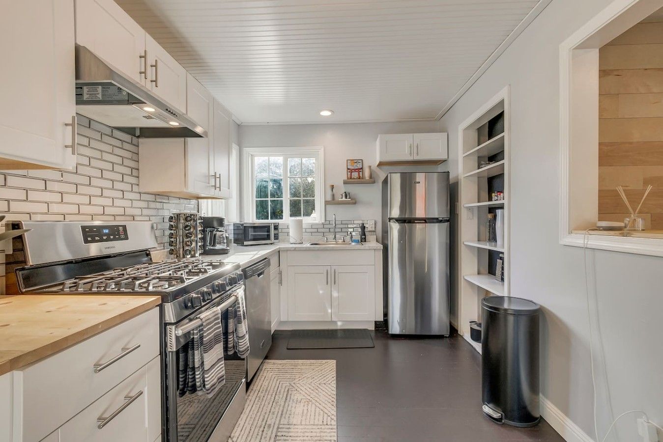 A modern kitchen with stainless steel appliances, white cabinetry, and a brick backsplash.