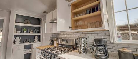 A modern kitchen with white cabinetry, a built-in stove, a coffee maker, and a window with a view.
