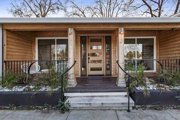 A modern wooden house with a front porch, a double door, and a small staircase leading to the entrance.