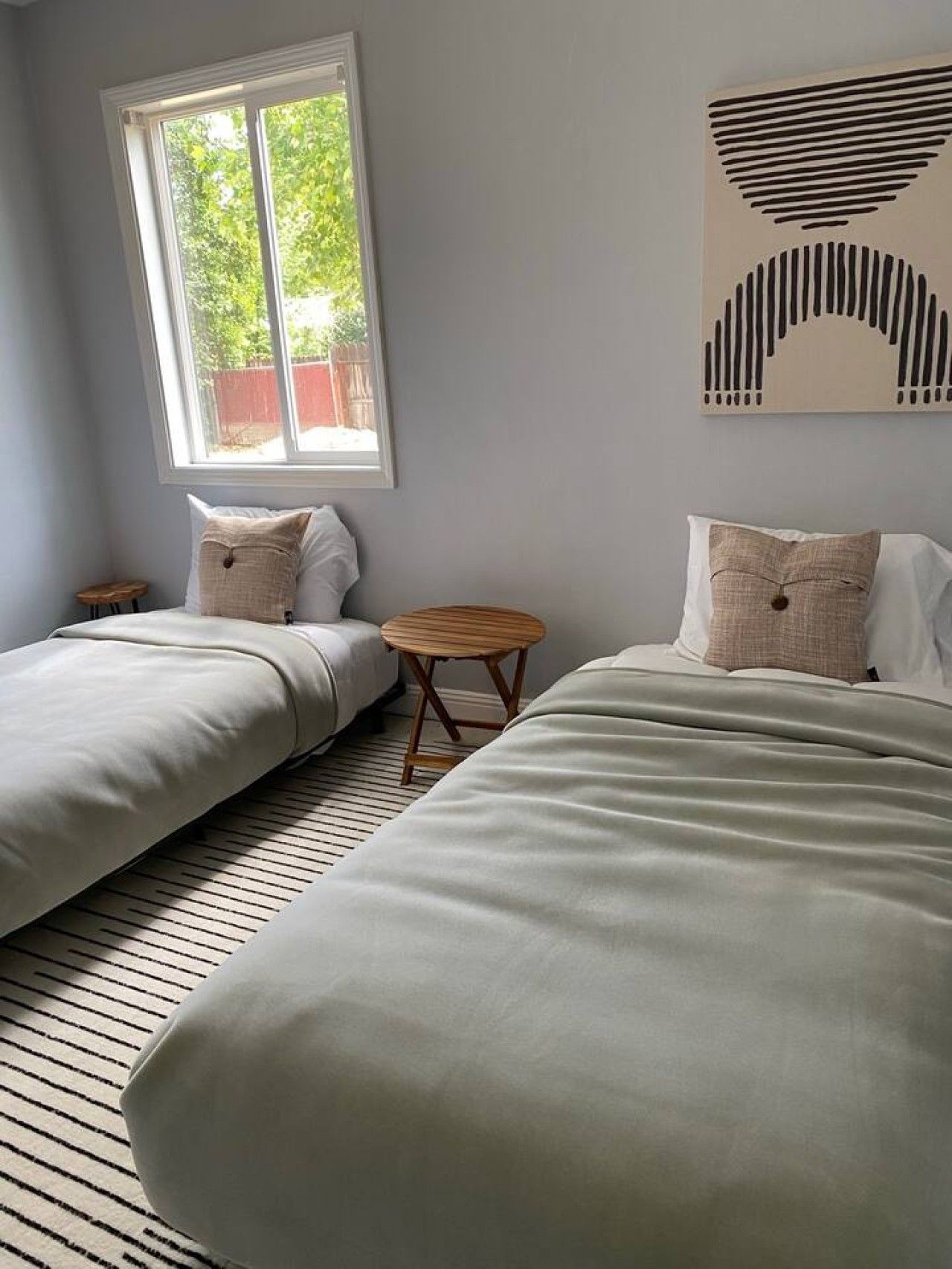 A room with two beds, a small round table, and a window with a view of greenery.