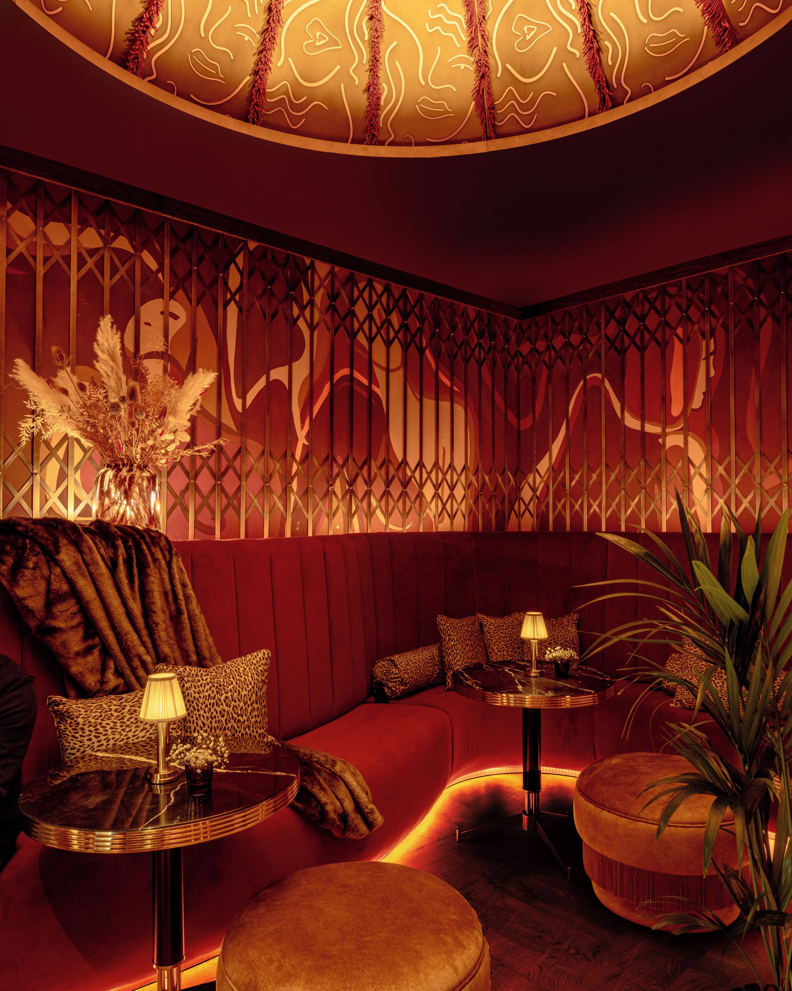 A dimly lit room with a red sofa, a round table with a lamp, and a decorative wall with a pattern.