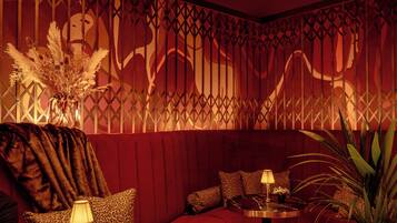 A dimly lit room with a red sofa, a round table with a lamp, and a decorative wall with a pattern.