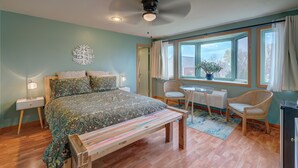 Une chambre à coucher comprenant un lit, des tables de chevet, un banc, une chaise, une petite table et une fenêtre avec des rideaux.