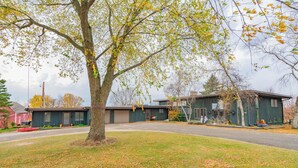 Un quartier résidentiel avec un grand arbre au premier plan, une maison avec un garage et un bâtiment rouge en arrière-plan.