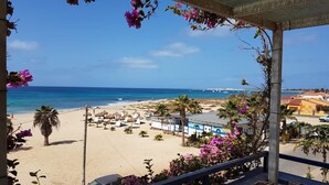 Vista de platja amb zona de piscina, palmeres i un edifici amb un rètol.