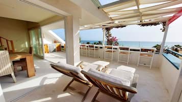 Ein Balkon mit Meerblick, eine Essecke mit Tisch und Stühlen sowie eine Küchenzeile mit Kühlschrank und Schränken.