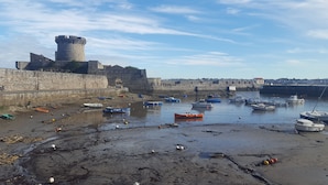 A coastal scene with a stone fortification, boats, and a sandy beach.