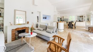 A spacious living area with a fireplace, a sofa, a dining table, and a kitchen in the background.