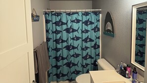 A bathroom with a shower curtain featuring shark prints, a toilet, a sink with toiletries, and a mirror. - Spacious five bedroom , 3 bathroom home . 1 mile from downtown Sturgis. (Sturgis)