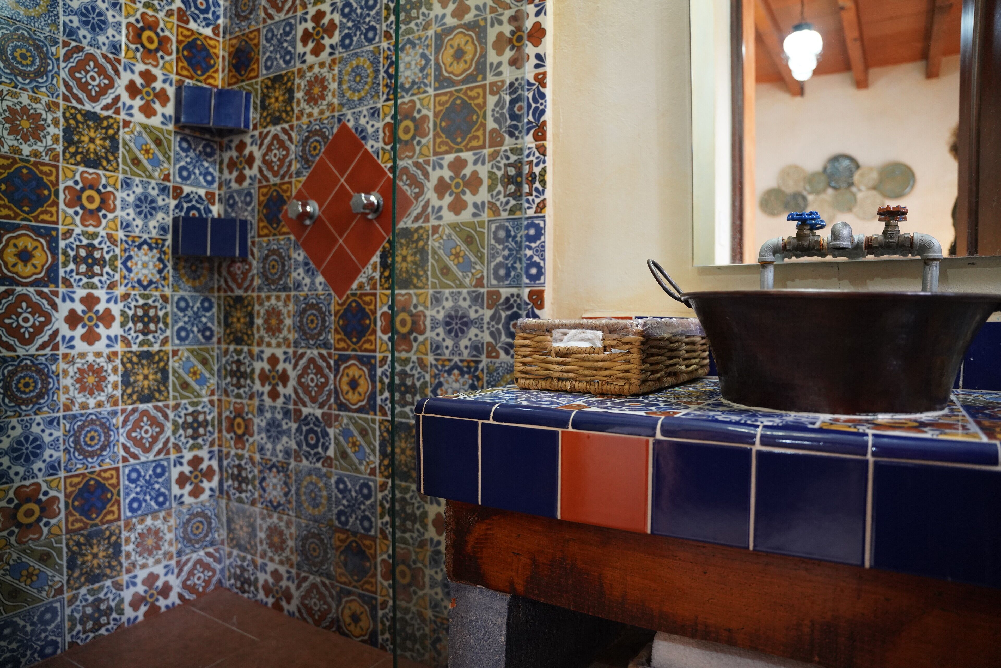 A bathroom with colorful tile walls and a sink area with a woven basket and a metal basin.