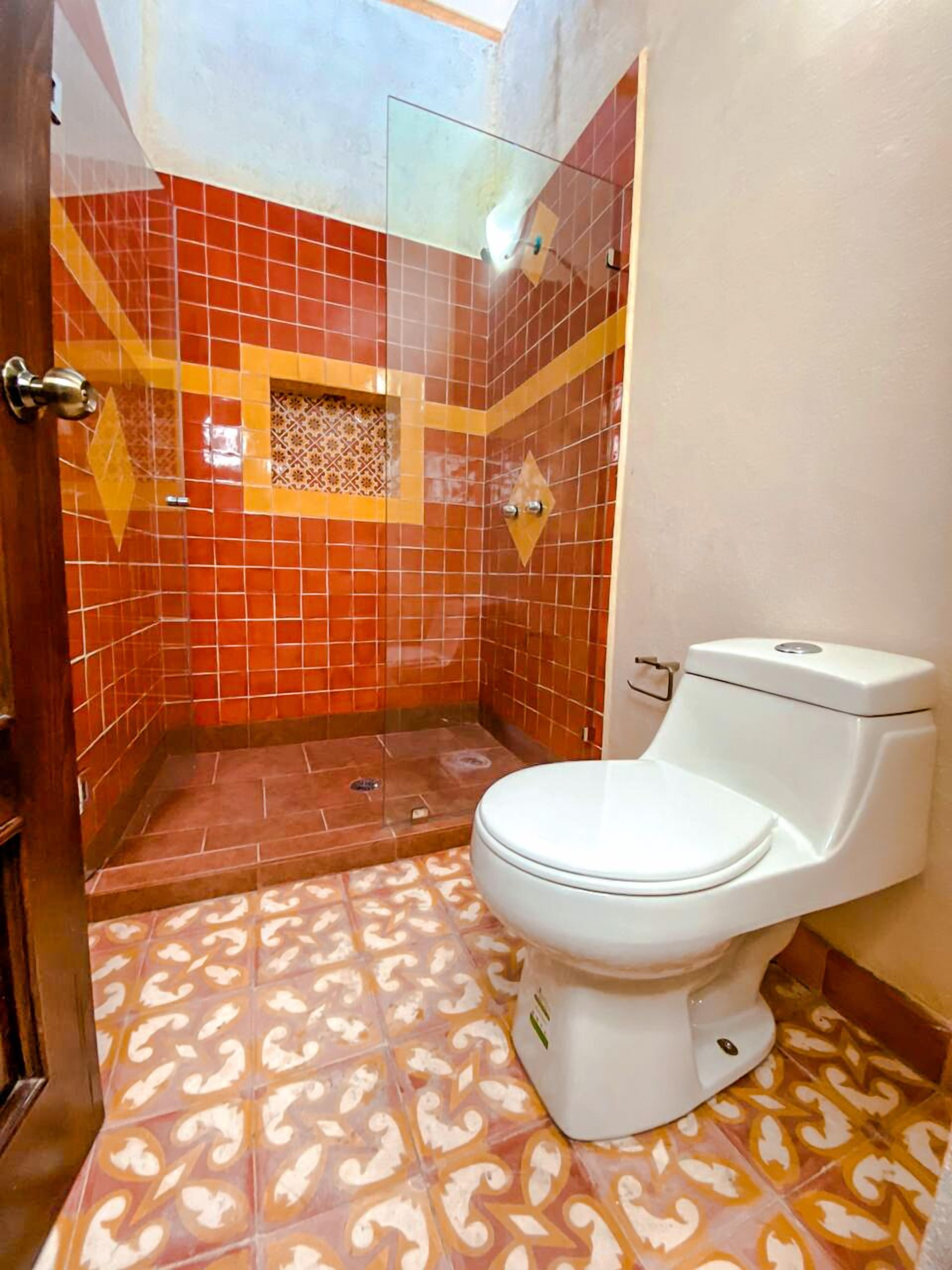 A bathroom with a white toilet, a shower enclosure, and patterned floor tiles.