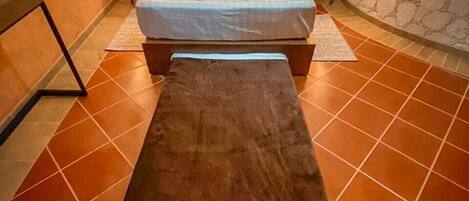A bedroom with a bed, a bench, and a stone wall.