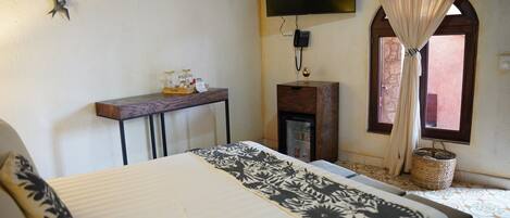 A bedroom with a bed, a desk, a TV, a window with curtains, and a wall-mounted phone.