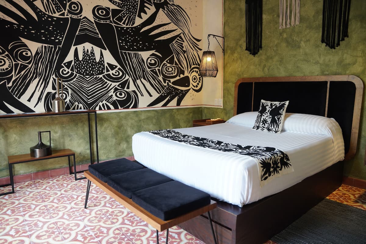 Een slaapkamer met een groot bed, een bankje, een muurschildering en een hanglamp.