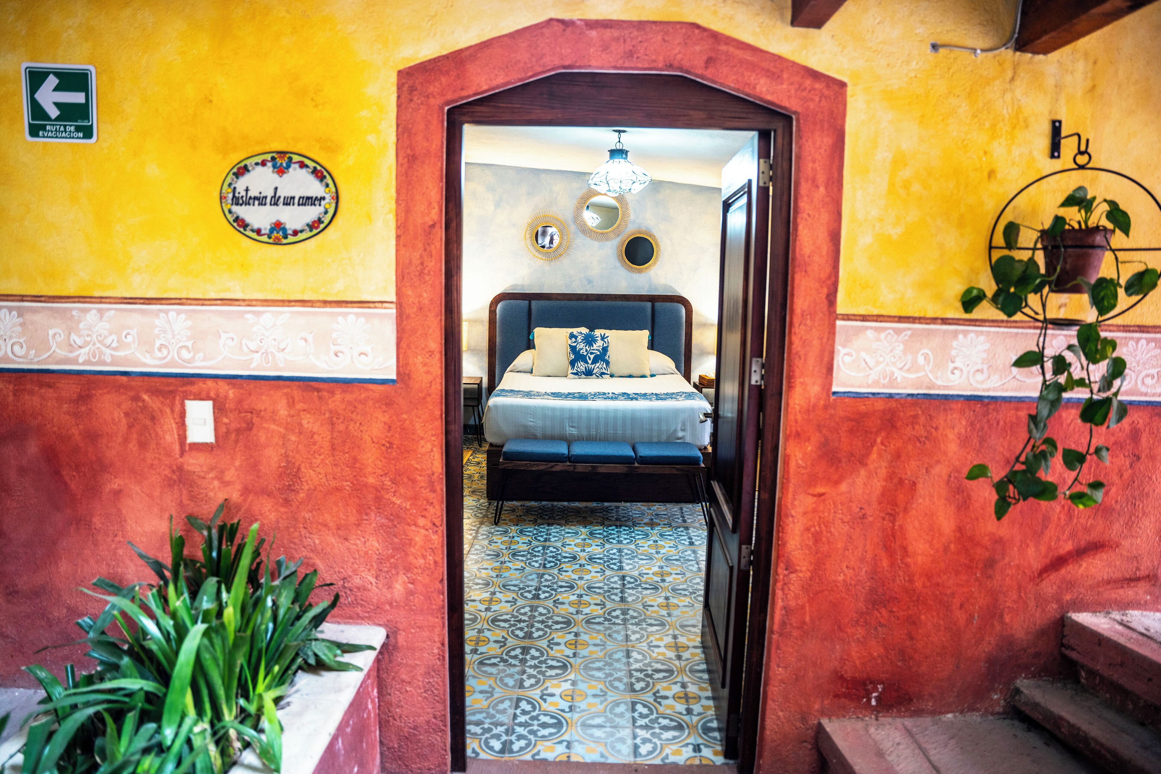 A narrow hallway leading to a bedroom with a bed, a potted plant, and a wall with a sign.
