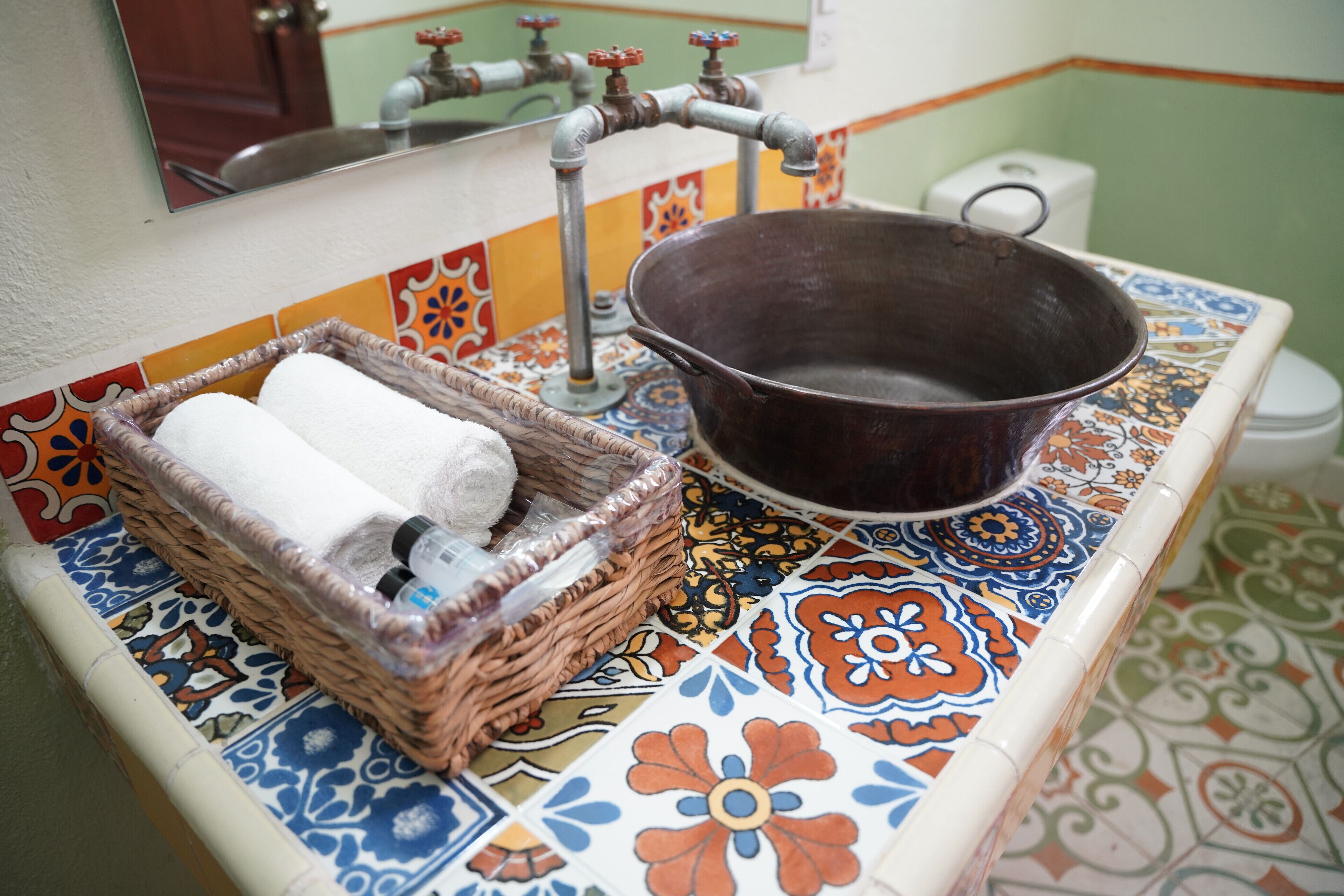 A bathroom with a colorful tile backsplash, a metal basin, and a wicker basket with towels.